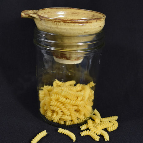Entonnoir jaune ancien avec marbrures posé sur un pot contenant des pâtes
